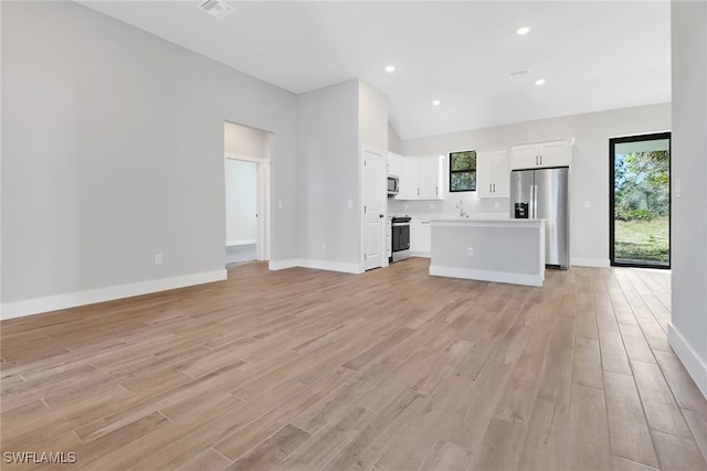 unfurnished living room featuring high vaulted ceiling, sink, light hardwood / wood-style floors, and a wealth of natural light