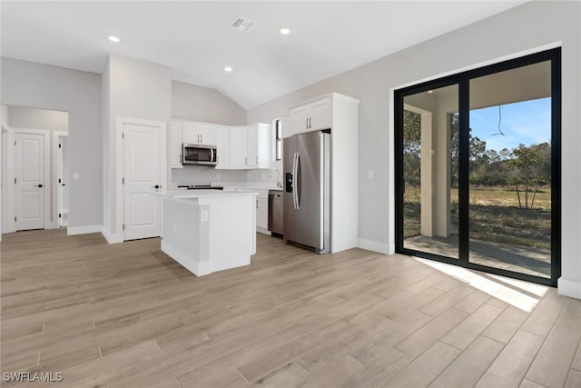 kitchen featuring appliances with stainless steel finishes, lofted ceiling, white cabinets, a center island, and light hardwood / wood-style floors