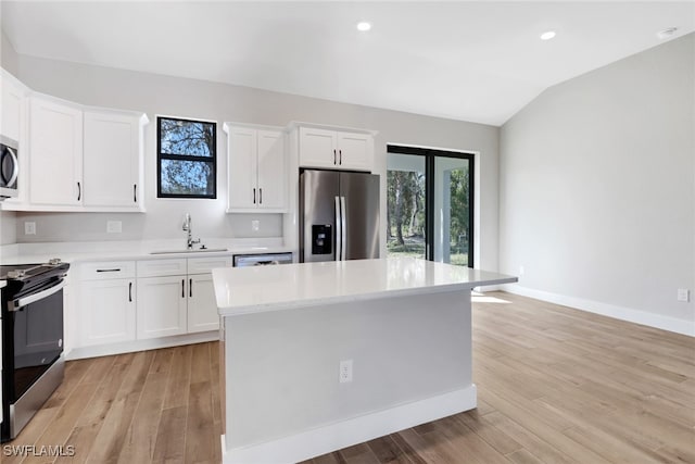 kitchen with sink, vaulted ceiling, a kitchen island, stainless steel appliances, and white cabinets