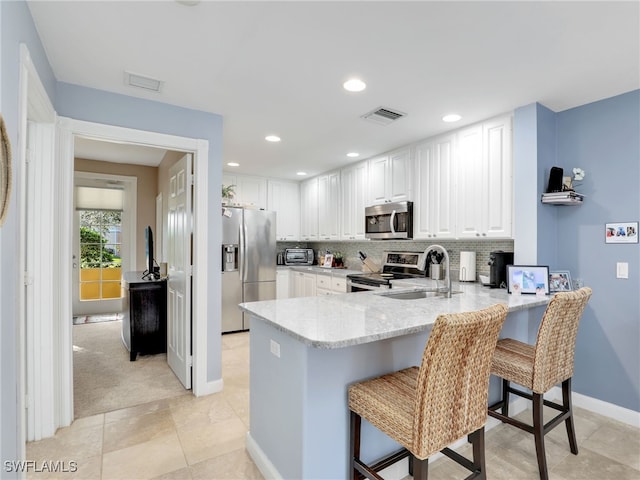 kitchen with sink, white cabinetry, a kitchen breakfast bar, stainless steel appliances, and kitchen peninsula