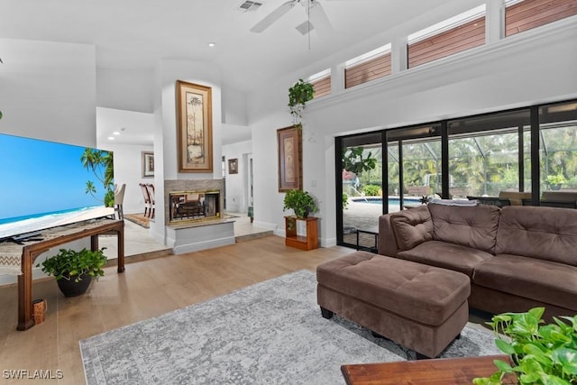 living room with ceiling fan, a multi sided fireplace, high vaulted ceiling, and light hardwood / wood-style flooring