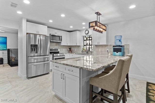 kitchen with appliances with stainless steel finishes, white cabinetry, a kitchen breakfast bar, decorative light fixtures, and kitchen peninsula