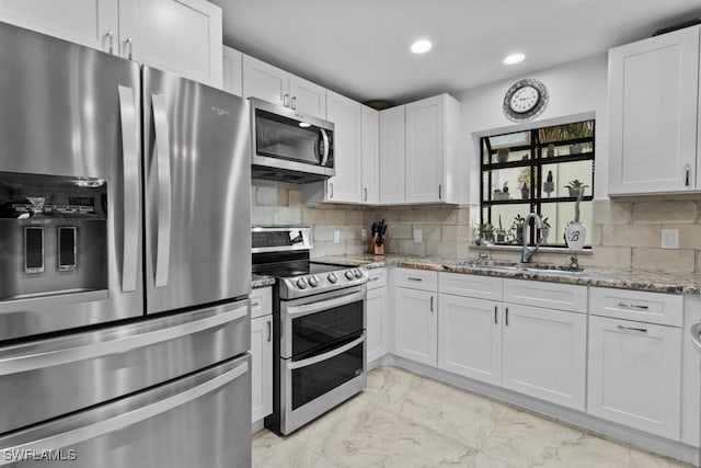 kitchen featuring appliances with stainless steel finishes, white cabinetry, sink, decorative backsplash, and light stone countertops