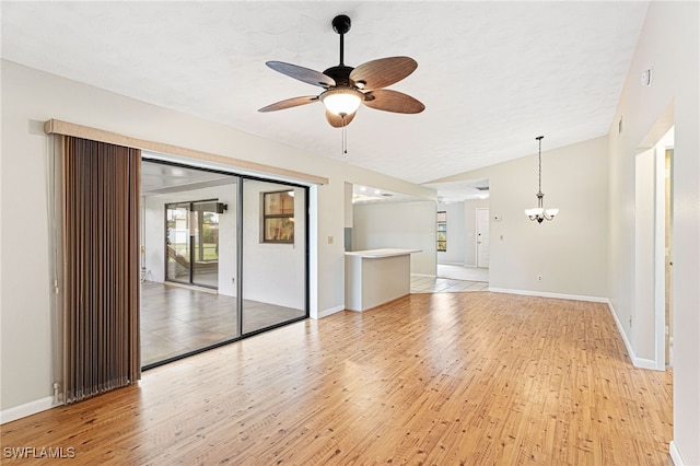 unfurnished living room with vaulted ceiling, ceiling fan with notable chandelier, and light wood-type flooring