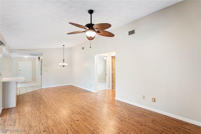 empty room with lofted ceiling, ceiling fan with notable chandelier, and light wood-type flooring