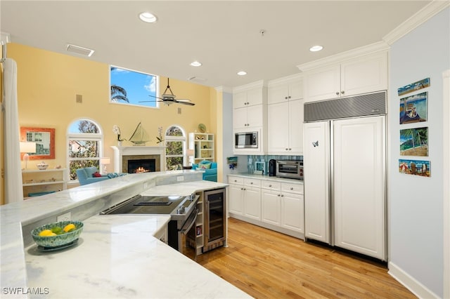 kitchen with white cabinetry, built in appliances, light hardwood / wood-style flooring, ceiling fan, and light stone countertops