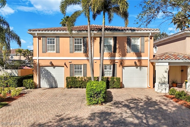 mediterranean / spanish-style home featuring decorative driveway, an attached garage, a tile roof, and stucco siding