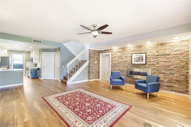 sitting room with light wood-style flooring, stairs, visible vents, and ceiling fan