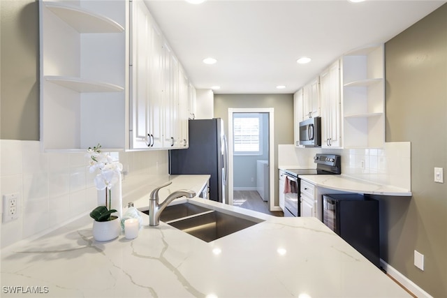 kitchen with stainless steel appliances, a sink, white cabinets, light stone countertops, and open shelves