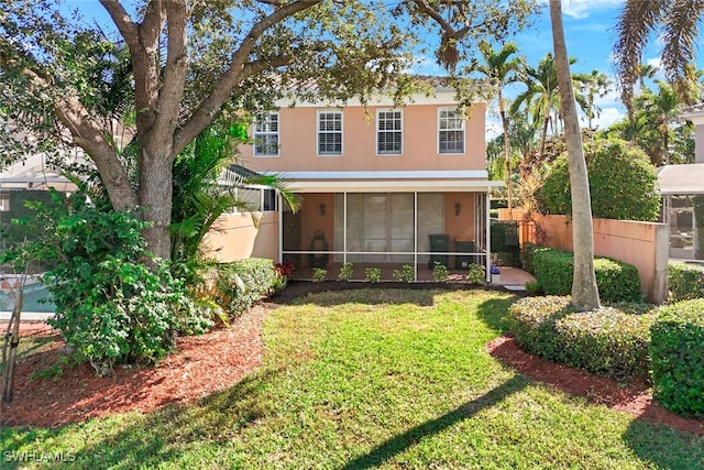 view of front of home featuring a front yard, a sunroom, fence, and stucco siding