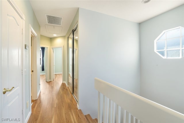 hallway with visible vents, light wood-style flooring, and an upstairs landing