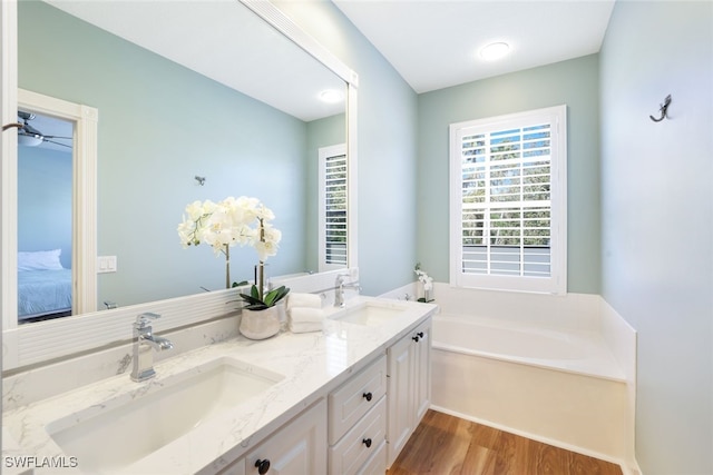 ensuite bathroom featuring a garden tub, double vanity, wood finished floors, and a sink