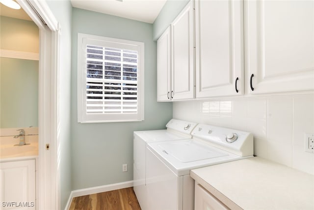 washroom with washing machine and clothes dryer, cabinet space, a sink, wood finished floors, and baseboards