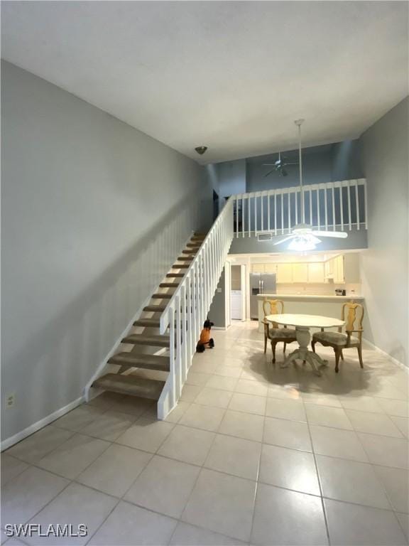 staircase featuring ceiling fan, tile patterned flooring, and a high ceiling