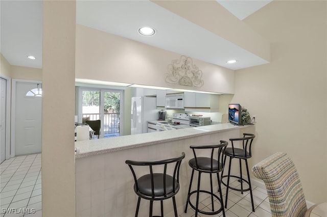 kitchen with light tile patterned flooring, white appliances, kitchen peninsula, and a breakfast bar area