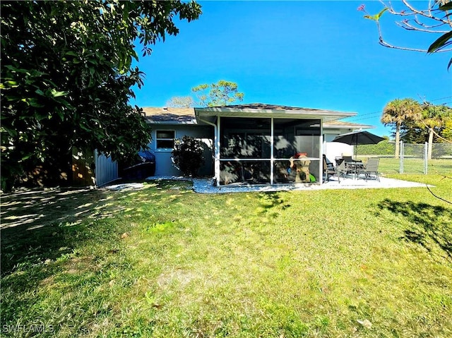 back of property with a sunroom, a patio area, and a lawn