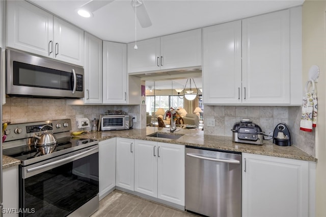 kitchen with stainless steel appliances, white cabinetry, light stone countertops, and sink