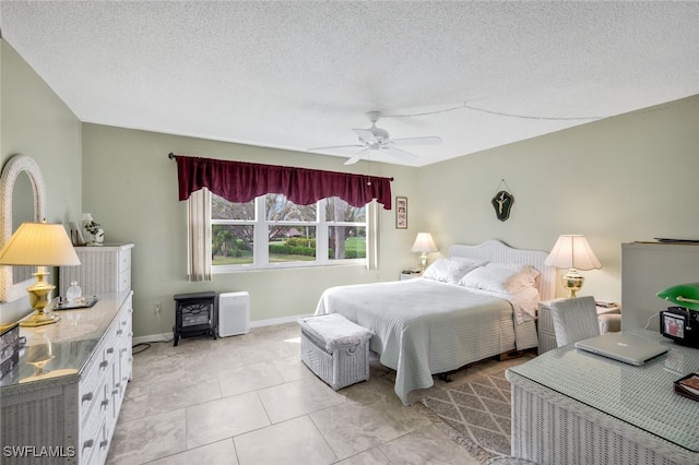 bedroom with ceiling fan, light tile patterned floors, a textured ceiling, and a wood stove