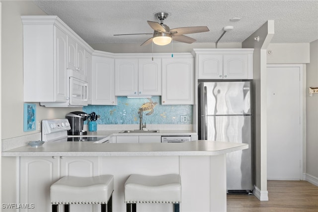 kitchen with white cabinetry, white appliances, kitchen peninsula, and sink