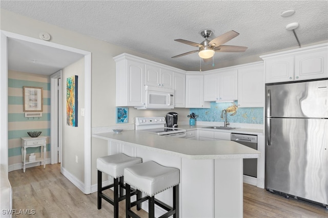 kitchen with sink, white cabinetry, appliances with stainless steel finishes, a kitchen breakfast bar, and light hardwood / wood-style floors