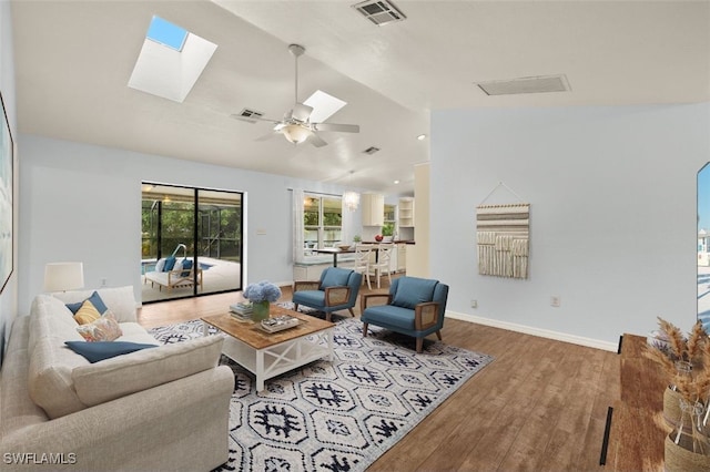 living room with hardwood / wood-style flooring, vaulted ceiling with skylight, and ceiling fan