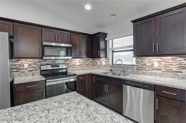 kitchen with dark brown cabinetry, sink, stainless steel appliances, and light stone countertops