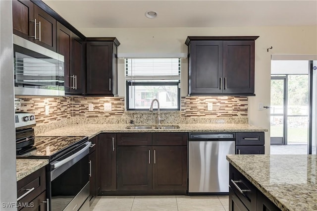 kitchen with dark brown cabinetry, appliances with stainless steel finishes, light stone countertops, and sink