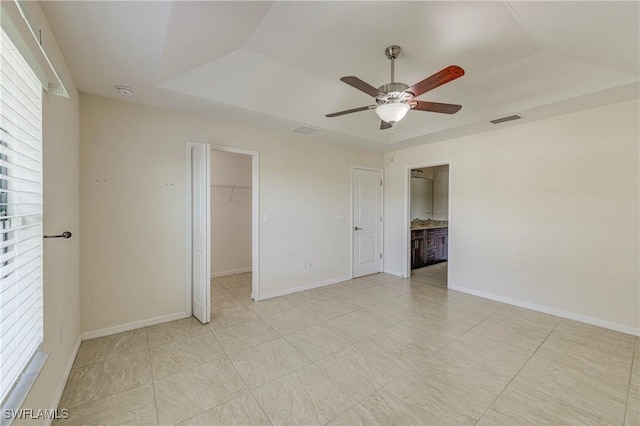 unfurnished bedroom featuring ensuite bathroom, a spacious closet, ceiling fan, a tray ceiling, and a closet