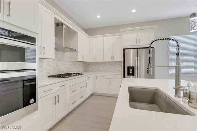 kitchen featuring wall chimney range hood, sink, white cabinets, and appliances with stainless steel finishes