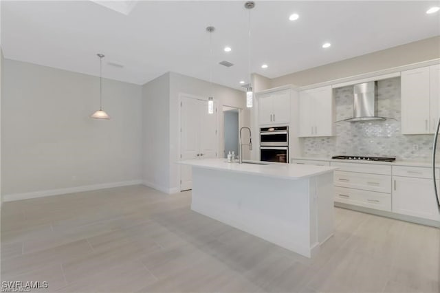 kitchen with black gas cooktop, white cabinetry, sink, a center island with sink, and wall chimney exhaust hood