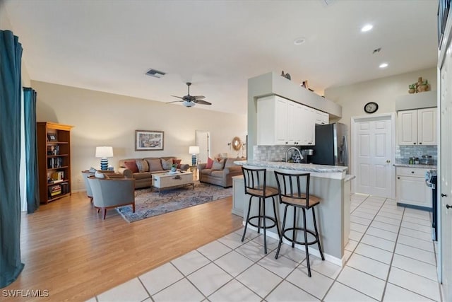 kitchen featuring a kitchen bar, kitchen peninsula, stainless steel fridge with ice dispenser, and white cabinets