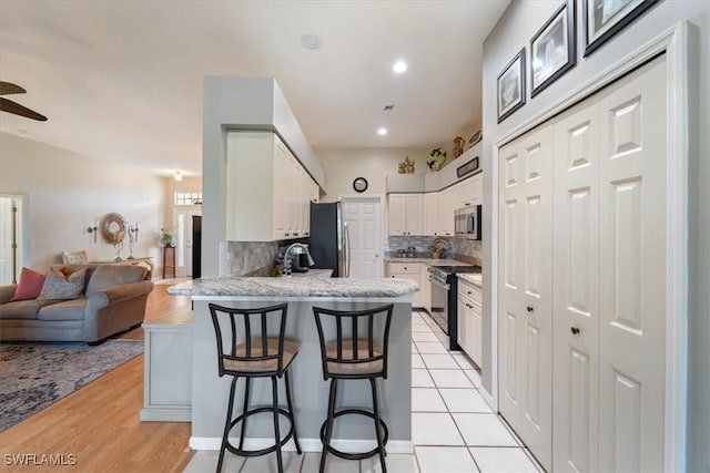 kitchen with a breakfast bar, white cabinetry, appliances with stainless steel finishes, kitchen peninsula, and backsplash