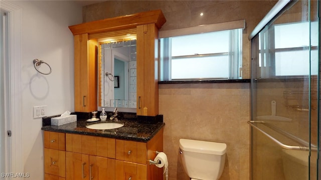 bathroom featuring vanity, toilet, a shower with shower door, and tile walls