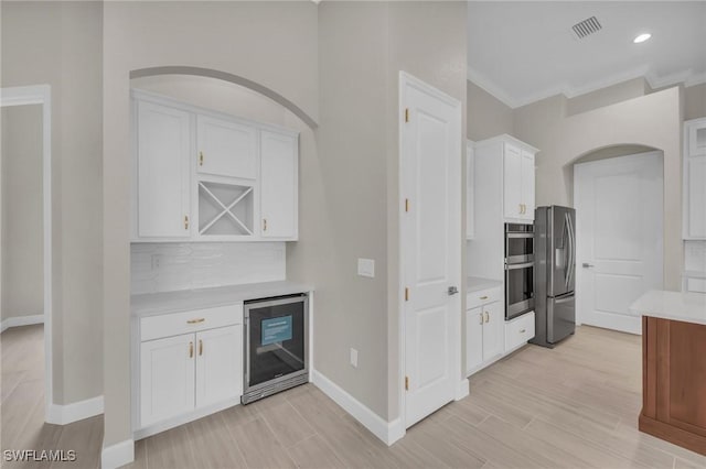 kitchen with tasteful backsplash, white cabinets, beverage cooler, stainless steel appliances, and crown molding