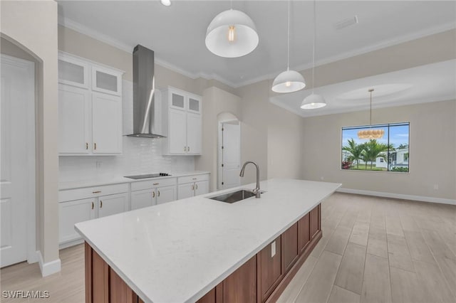 kitchen featuring wall chimney range hood, hanging light fixtures, sink, and white cabinets