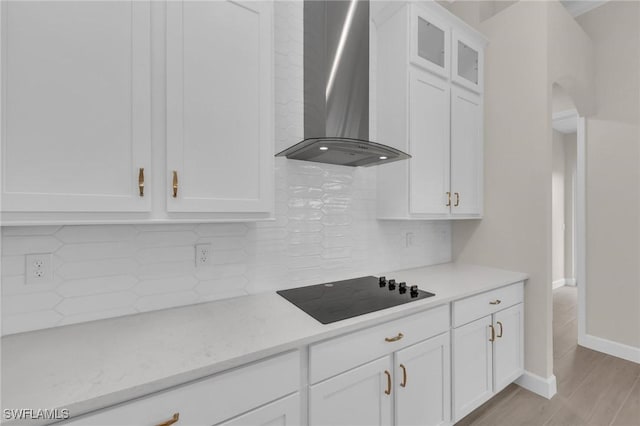 kitchen featuring white cabinets, decorative backsplash, black electric cooktop, wall chimney range hood, and light wood-type flooring