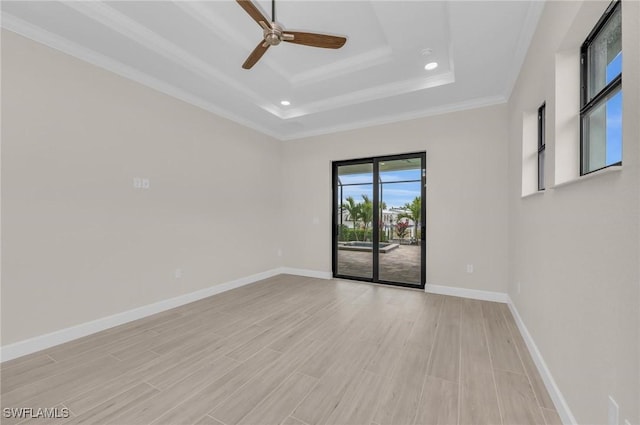 empty room with ornamental molding, light hardwood / wood-style flooring, ceiling fan, and a tray ceiling