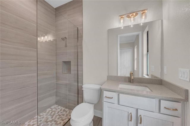 bathroom featuring a tile shower, vanity, and toilet