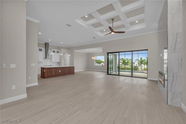 unfurnished living room with a towering ceiling, a large fireplace, coffered ceiling, ceiling fan, and light hardwood / wood-style floors