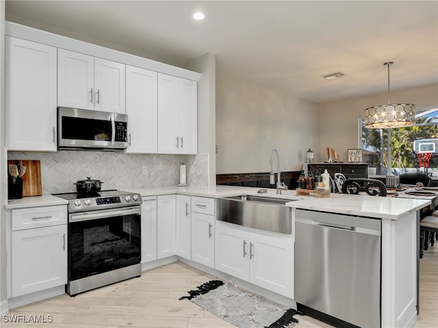 kitchen with decorative light fixtures, sink, white cabinets, kitchen peninsula, and stainless steel appliances