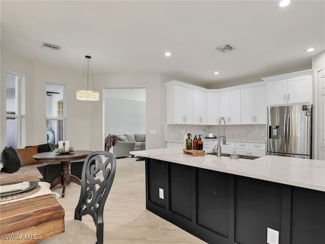 kitchen featuring light stone counters, stainless steel fridge with ice dispenser, white cabinetry, and sink