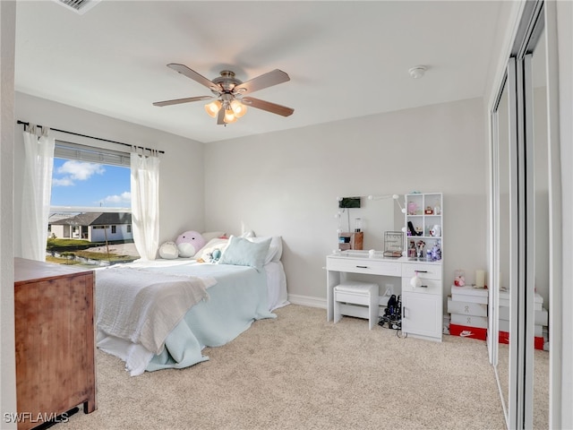 bedroom featuring light colored carpet, ceiling fan, and a closet