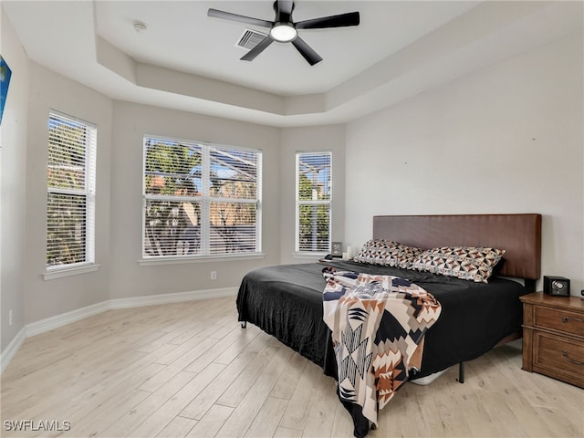 bedroom with ceiling fan, a tray ceiling, and light hardwood / wood-style floors