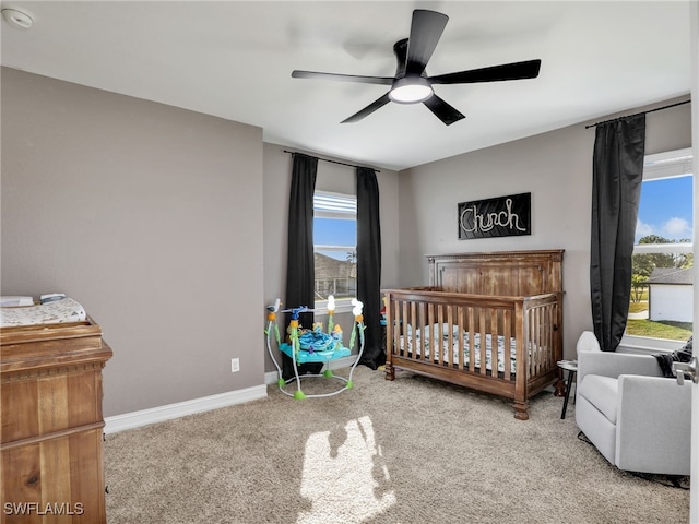 bedroom featuring a nursery area, ceiling fan, and carpet