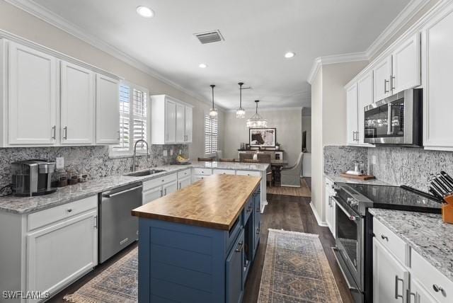 kitchen with appliances with stainless steel finishes, wood counters, white cabinetry, sink, and a center island