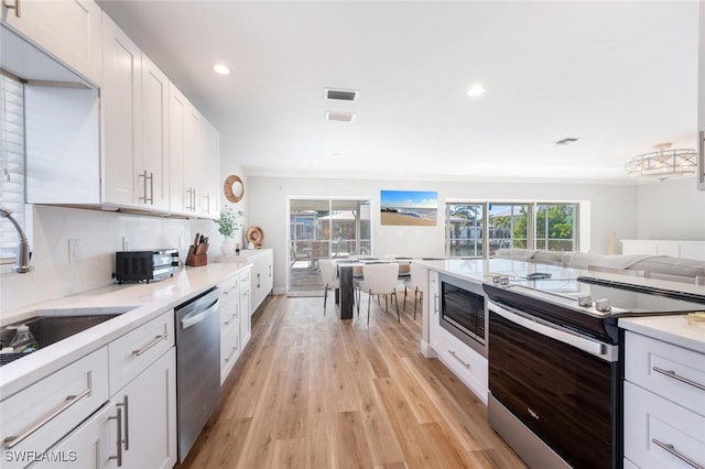 kitchen featuring visible vents, light wood-type flooring, white cabinets, stainless steel appliances, and a sink