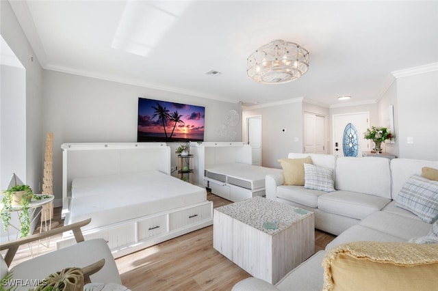 living area with an inviting chandelier, visible vents, light wood finished floors, and ornamental molding