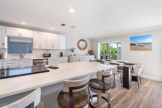 kitchen featuring light wood-type flooring, a sink, a breakfast bar area, light stone countertops, and dishwasher