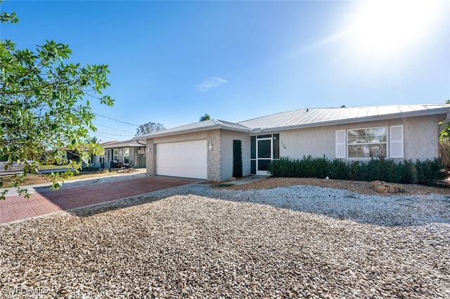 ranch-style home with decorative driveway, metal roof, an attached garage, and stucco siding