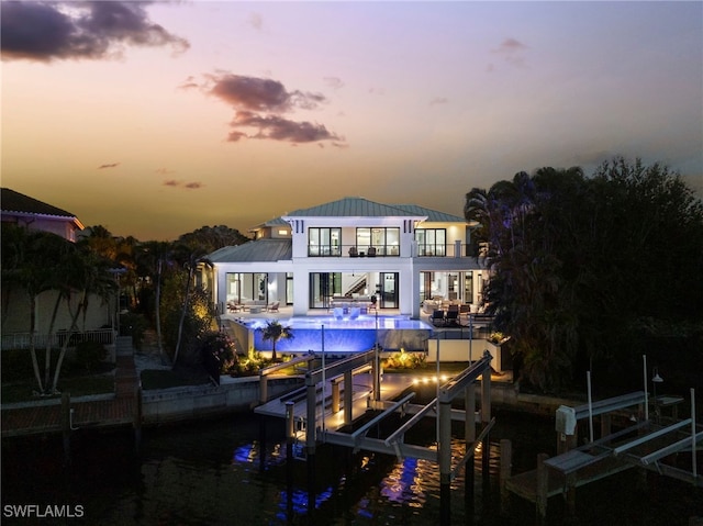 back house at dusk featuring a water view, a balcony, and a patio